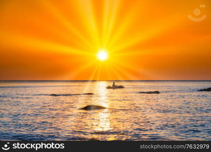 Sunset sea and beach with rocks with silhouette of fisherman on boat and sunset sun on dramatic sky