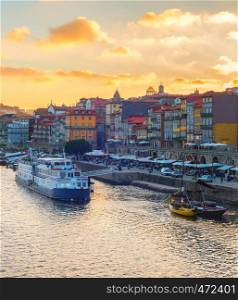 Sunset sky above Porto skyline, embankment with tour boats and wine ships at Douro river, tourists walking and sitting in restaurants of historical downtown, Portugal