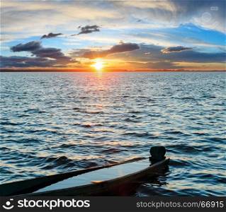 Sunset sky and old drowned wooden fishing boat on summer lake bank.