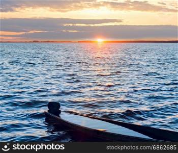 Sunset sky and old drowned wooden fishing boat on summer lake bank.