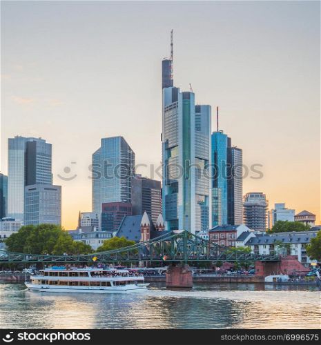 Sunset sky over city embankment, touristic boats and bridge by Frankfurt skyline with modern architecture, Germany