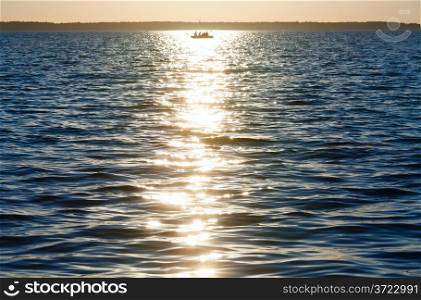 Sunset, sun track and fishing boat on summer lake surface.