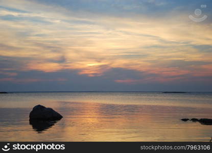 Sunset view by rocks in the colorful and reflecting water