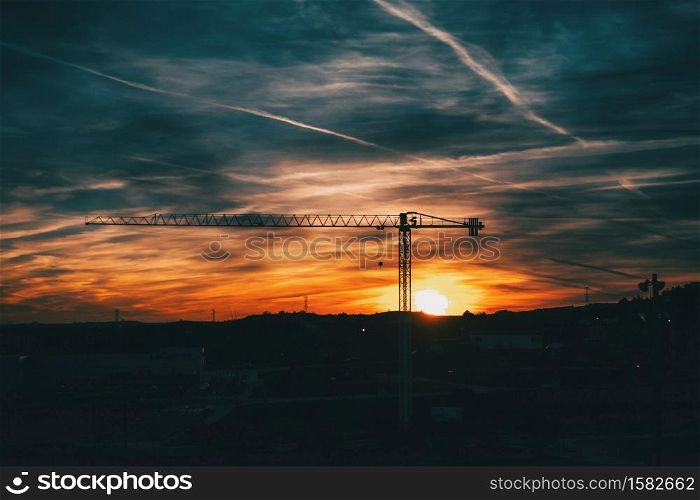 Sunset with blue and orange clouds with the silhouette of a construction crane in the center