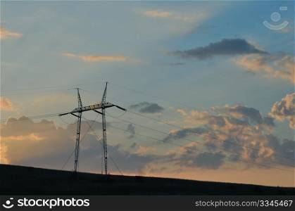 Sunset with high voltage electric pylon in field