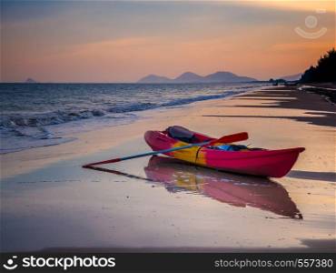 Sunset with orange afernoon sky over sea with kayak boat on beach with reflection, Thailand