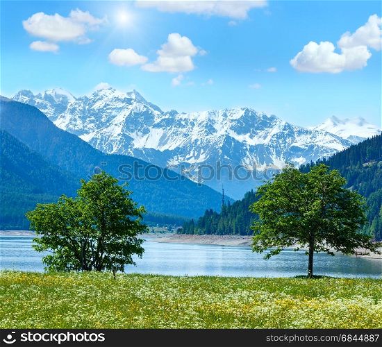 Sunshiny Reschensee ( or Lake Reschen) summer landscape with blossoming meadow and blue cloudy sky (Italy)