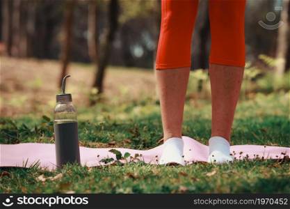 Super close up of two legs over a yoga mat with a bottle of water with copy space at the park