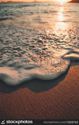 Super close up shot of a tide with a lot of foam over the sand of the beach