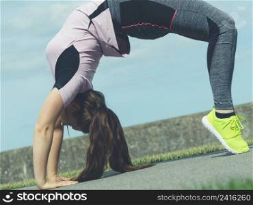 Super fit attractive young woman wearing fashionable outfit working out being active outside during sunny weather. Stretching her back or practice yoga. Woman doing yoga outdoor