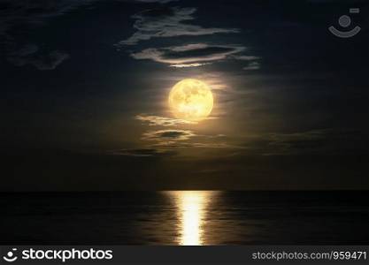 Super full moon and cloud in the yellow sky above the ocean horizon at midnight, moonlight reflect the water surface and wave, Beautiful nature landscape view at night scene of the sea for background. View at night scene of the sea