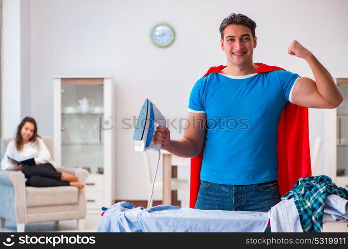 Super hero man husband ironing at home helping his wife