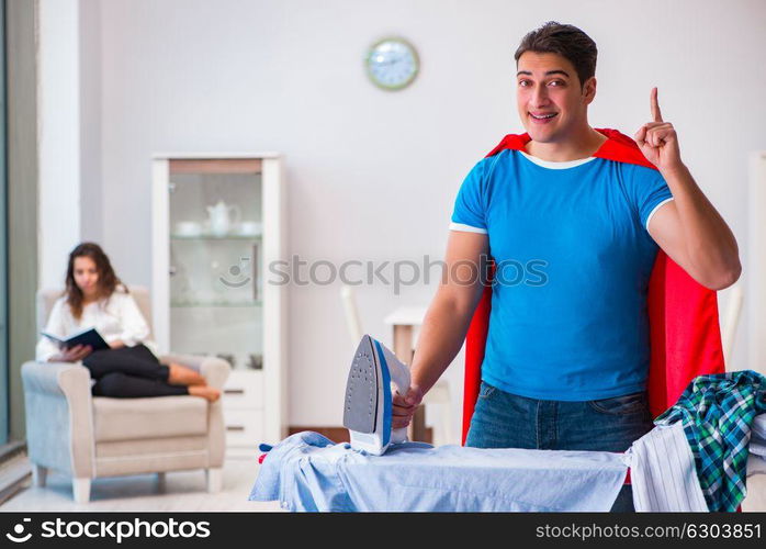 Super hero man husband ironing at home helping his wife