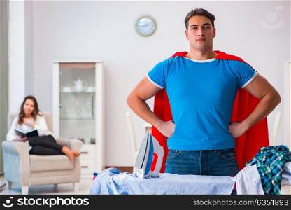 Super hero man husband ironing at home helping his wife
