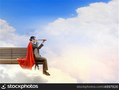 Super hero sitting on bench and looking in spyglass. Guy in super hero costume