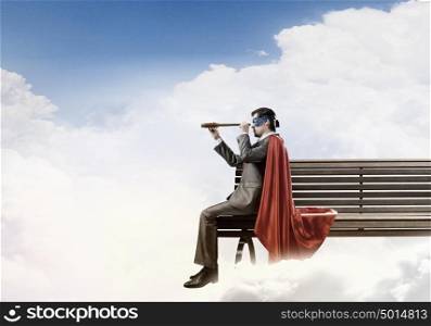 Super hero sitting on bench and looking in spyglass. Guy in super hero costume