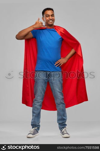 super power and people concept - happy smiling indian man in red superhero cape making phone call gesture over grey background. indian man in superhero cape making call gesture