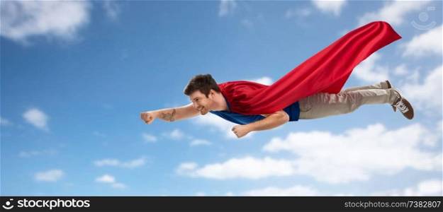 super power and people concept - happy young man in red superhero cape flying in air over blue sky and clouds background. man in red superhero cape flying over sky