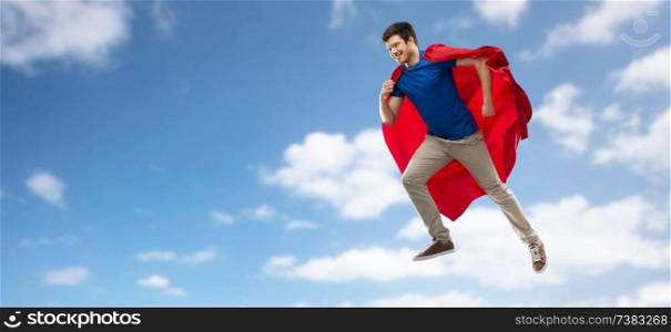 super power and people concept - happy young man in red superhero cape flying in air over blue sky and clouds background. man in red superhero cape flying over sky
