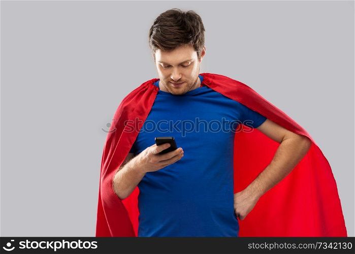 super power, technology and people concept - young man in red superhero cape using smartphone over grey background. young man in red superhero cape using smartphone