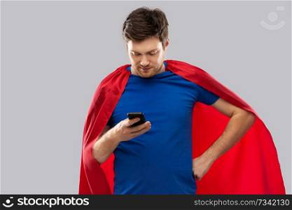 super power, technology and people concept - young man in red superhero cape using smartphone over grey background. young man in red superhero cape using smartphone