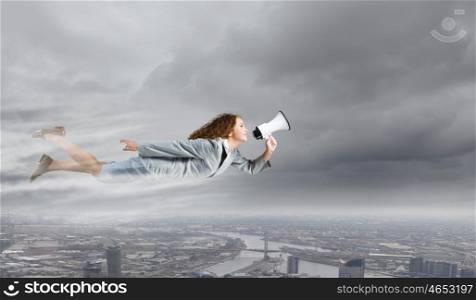 Super woman. Young businesswoman with megaphone flying high in sky