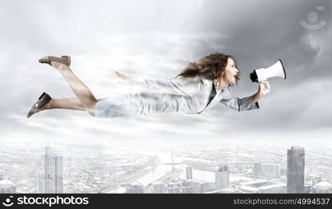 Super woman. Young businesswoman with megaphone flying high in sky