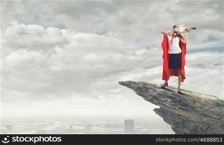 Super woman. Young confident woman in red cape and mask playing violin