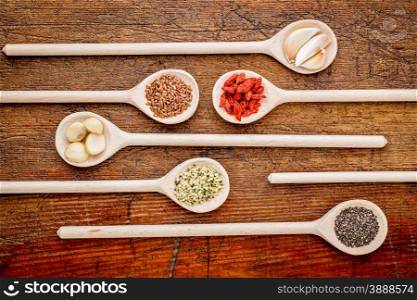 superfood abstract (garlic cloves, goji berry, chia, hemp, flax seeds, macadamia,nuts) - top view of wooden spoons against rustic grunge wood
