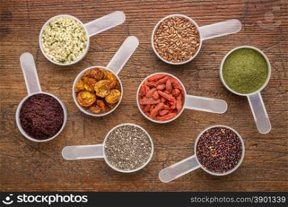 superfood abstract (wheatgrass, acai berry, goji berry, falx seed,chia seed,goldenberry,hemp seed, quinoa grain) - top view of measuring scoop against rusti wood