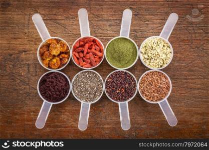 superfood abstract (wheatgrass, acai berry, goji berry, flax seed,chia seed, goldenberry, hemp seed, quinoa grain) - top view of measuring scoop against rustic wood