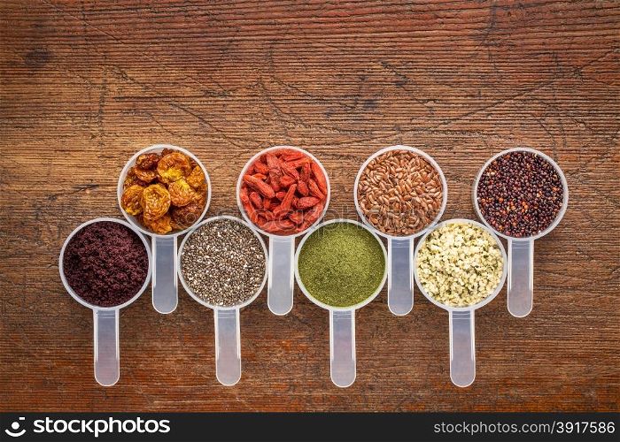 superfood abstract (wheatgrass, acai berry, goji berry, flax seed,chia seed,goldenberry, hemp seed, quinoa grain) - top view of measuring scoop against rustic wood with a copy space