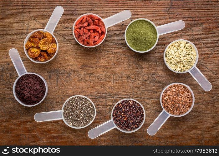superfood abstract (wheatgrass, acai berry, goji berry, flax seed,chia seed,goldenberry,hemp seed, quinoa grain) - top view of measuring scoops surrounding a copy space on a rustic wood