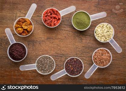 superfood abstract (wheatgrass, acai berry, goji berry, flax seed,chia seed,goldenberry,hemp seed, quinoa grain) - top view of measuring scoops surrounding a copy space on a rustic wood
