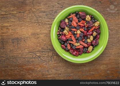 superfruit berry mix (blueberry, mulberry, cherry, goji, elderberry, chokeberry, and cranberry) - green ceramic bowl against grunge wood