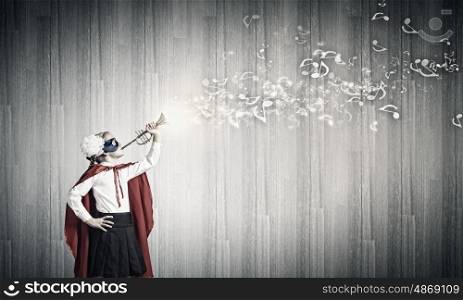 Superkid with trumpet. Cute girl of school age in superhero costume playing trumpet
