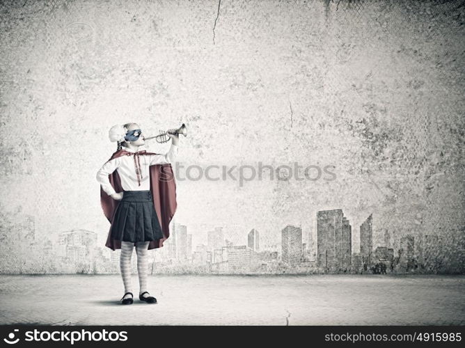 Superkid with trumpet. Cute girl of school age in superhero costume playing trumpet