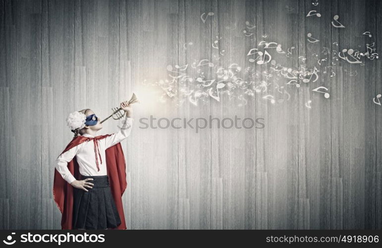 Superkid with trumpet. Cute girl of school age in superhero costume playing trumpet