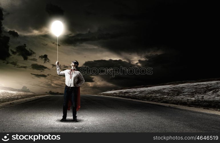 Superman with balloon. Young man in superhero costume holding balloon in hand