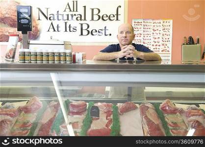 Supermarket employee stands at meat counter in supermarket