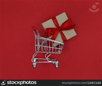Supermarket trolley and gift box on red background. Shopping concept.. Supermarket trolley and gift box on a red background. Shopping concept.