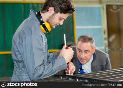 supervisor checking the work of an apprentice engineer in factory