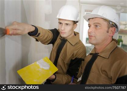 supervisor overseeing apprentice using filler on plasterboard