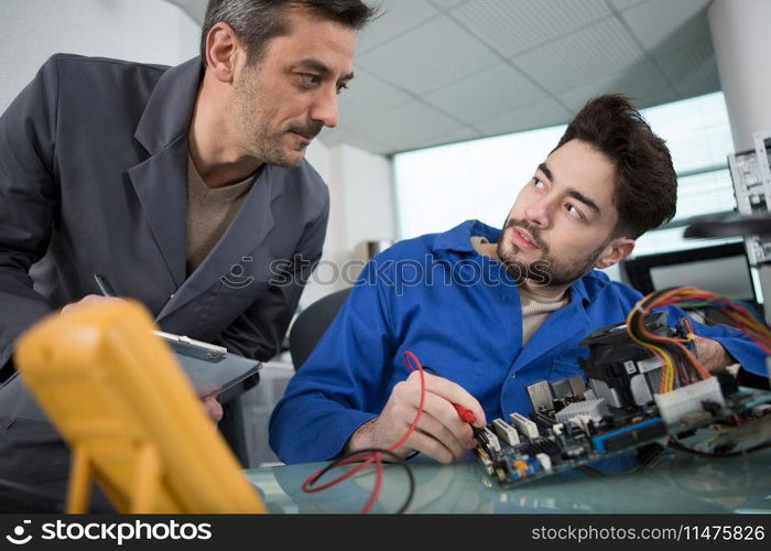 supervisor talking to electronics apprentice using multimeter