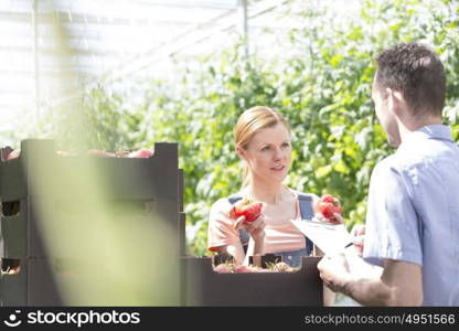 Supervisor talking to woman while examining tomatoes at greenhouse