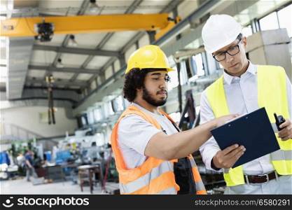 Supervisor with manual worker discussing over clipboard in metal industry