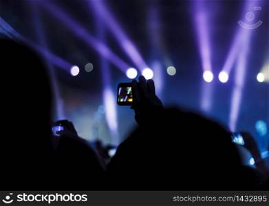Supporters recording at concert - Candid image of crowd at rock concert. Silhouettes of people and musicians in big concert stage
