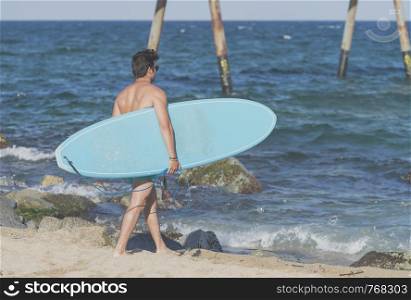 Surfer carrying his blue surfboard from behind