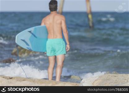 Surfer carrying his blue surfboard from behind