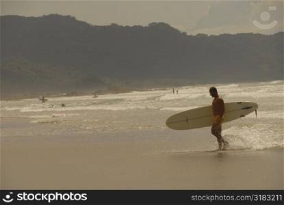 Surfer carrying his surfboard on beach in Costa Rica